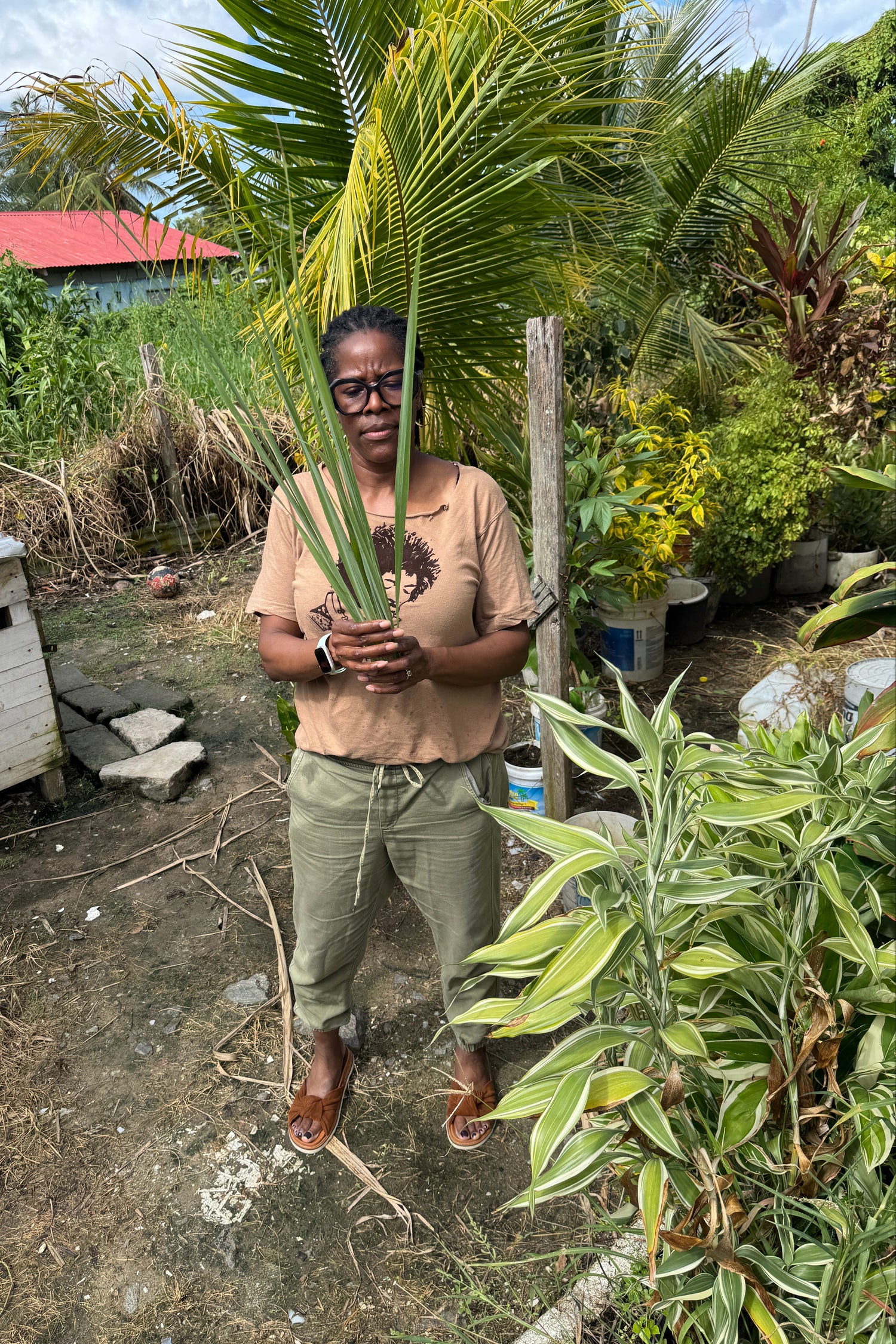 Person holding a leaf in a natural outdoor setting with greenery and a wooden structure.