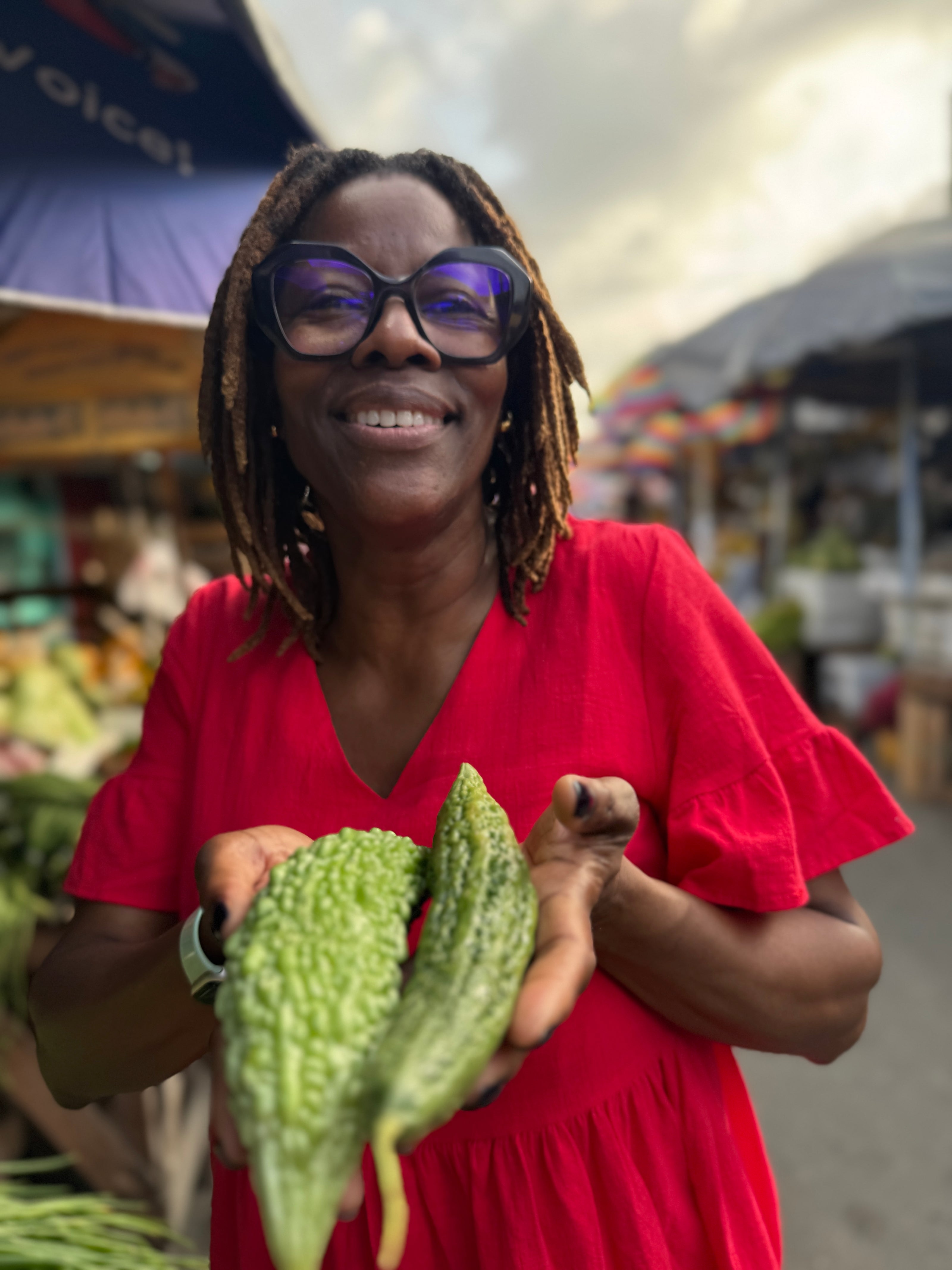Woman in a red dress holding a bitter melon at an outdoor market.