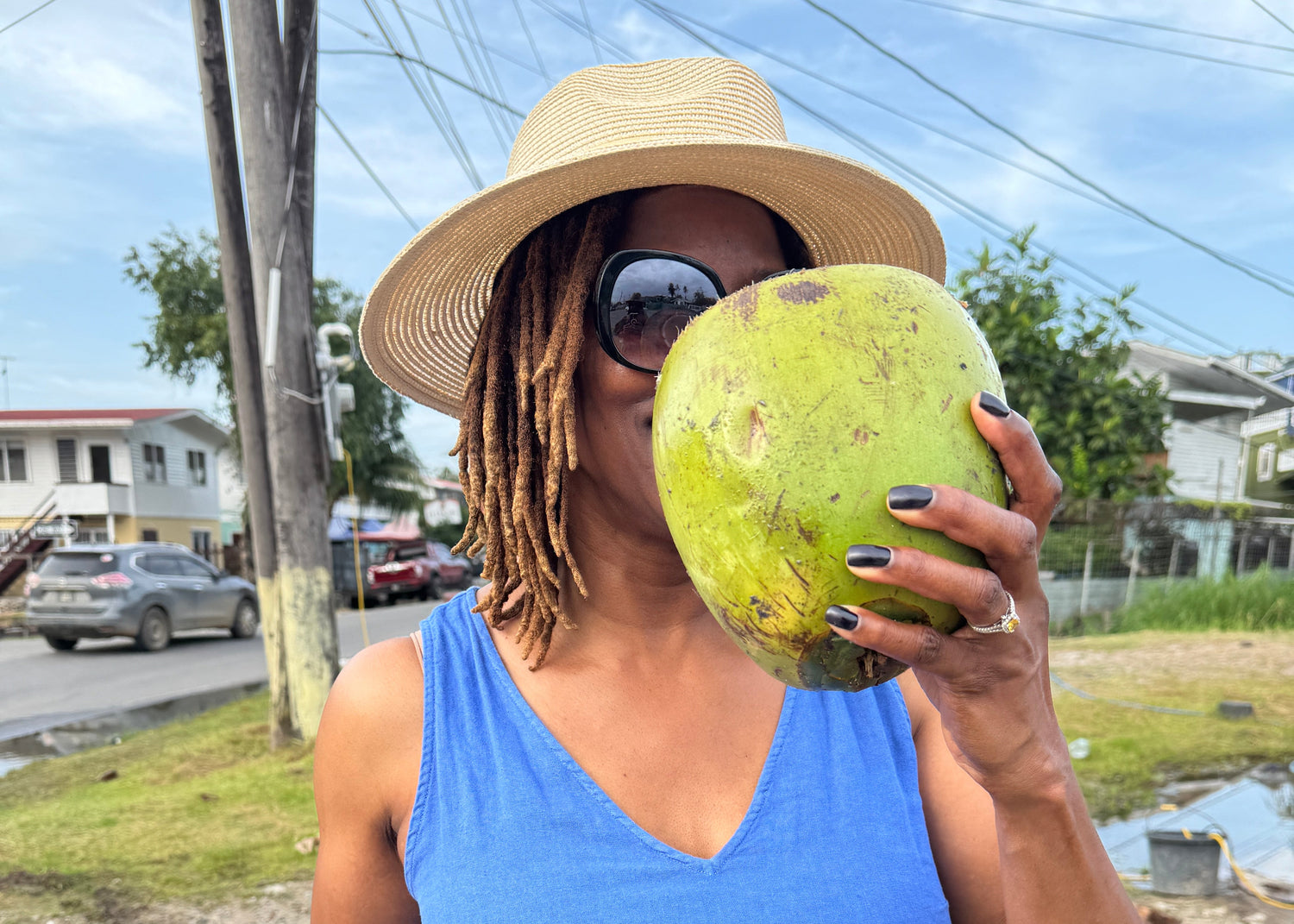 Person holding a green coconut outdoors with buildings and power lines in the background