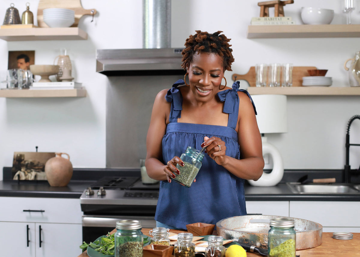 Woman in a kitchen preparing food, holding a jar of green liquid.