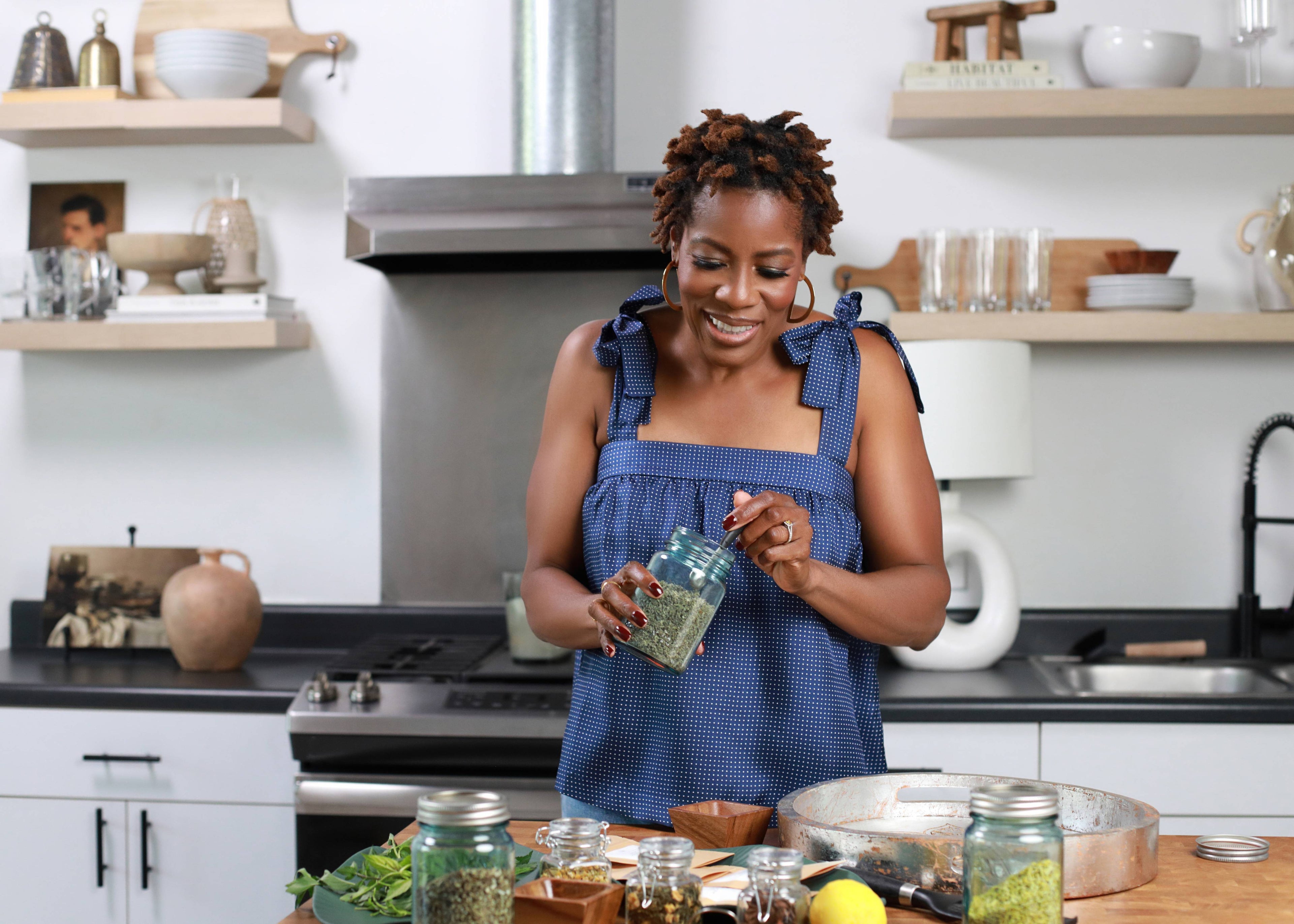 Woman in a kitchen preparing food, holding a jar of green liquid.